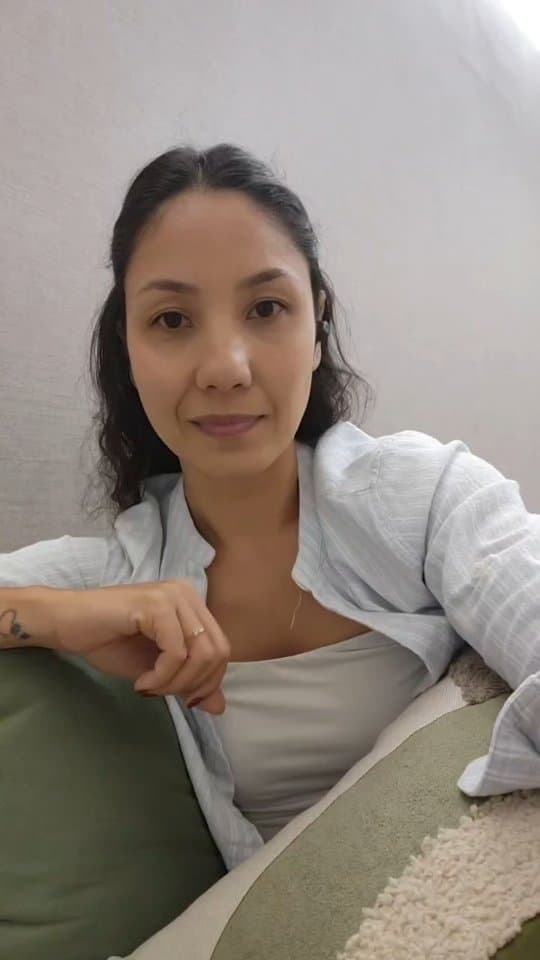 Gatana sentada no sofá verde do consultório, gravando um vídeo