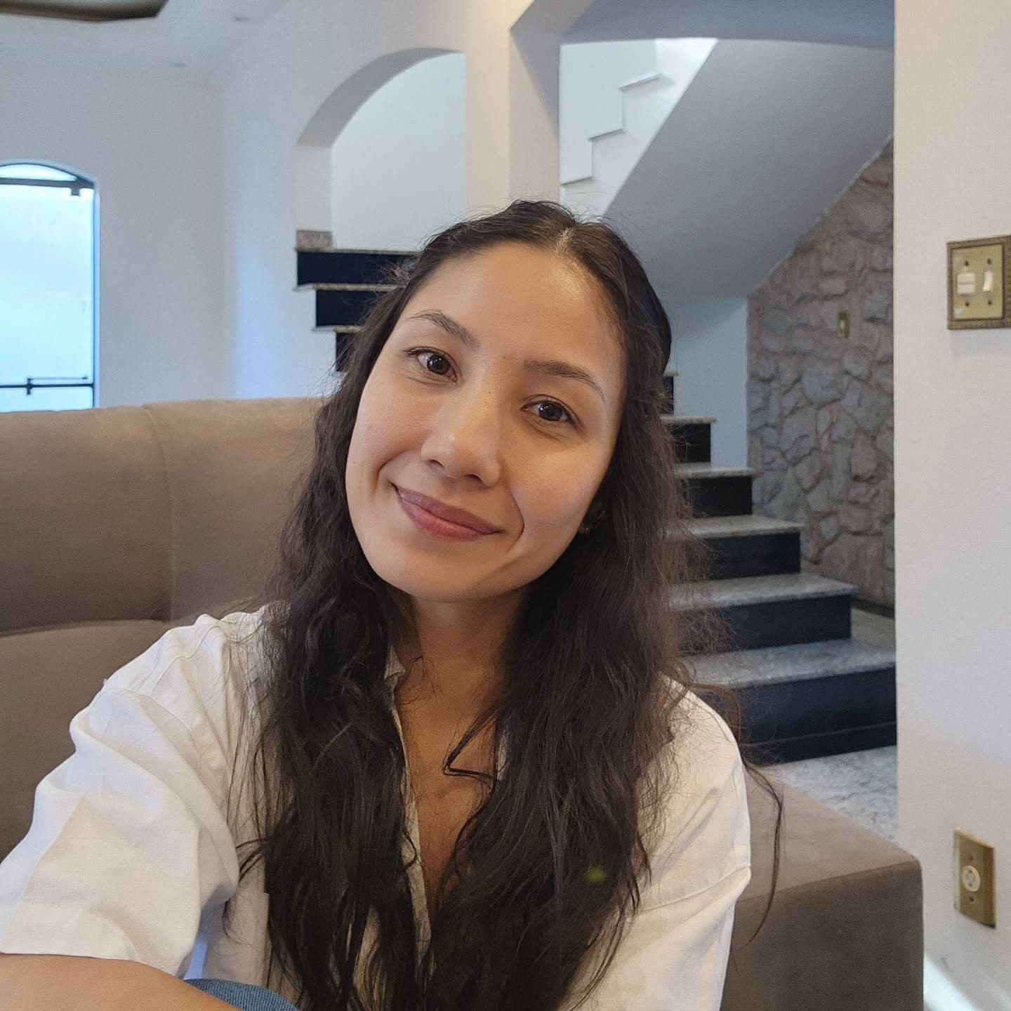 Gatana Cavalhieri sorrindo, de camisa branca, sentada num sofá